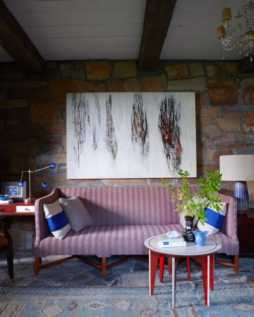 Interior view of a living room with a striped sofa, round accent table, and stone wall, illuminated by natural light.