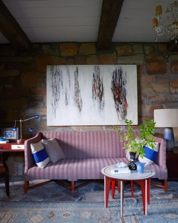 Interior view of a living room with a striped sofa, round accent table, and stone wall, illuminated by natural light.