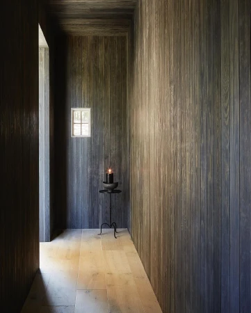 Interior hallway with wood-paneled walls and floor, a small window, and a minimalist candle stand creating a serene and modern atmosphere.