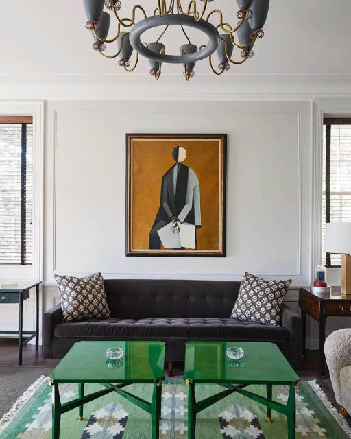 Living room interior with gray sofa, green coffee tables, patterned rug, framed painting, and stylish lighting fixture on the ceiling.