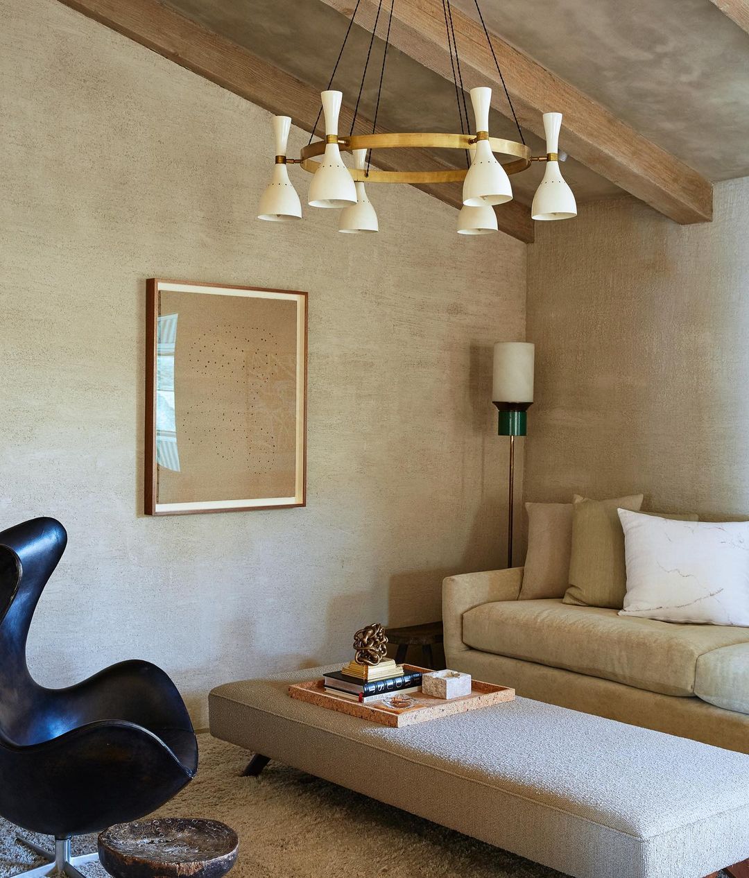 Living room interior with a mid-century modern chandelier, black swan chair, neutral sofa, ottoman, framed art, and warm beige color palette.