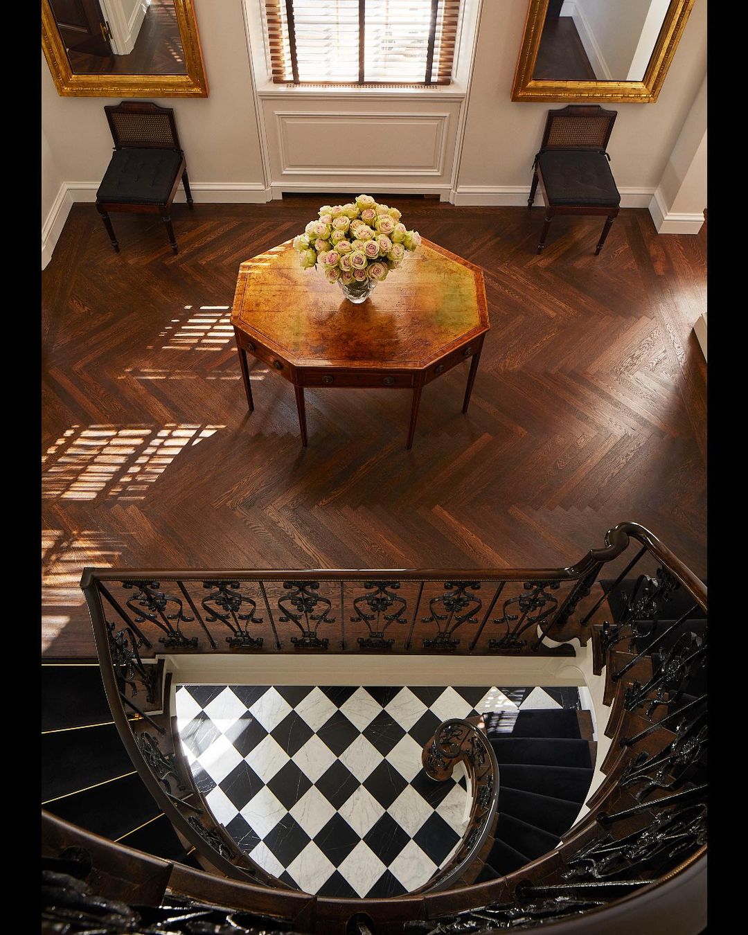 Overhead shot of a grand entryway with dark wood floors, a spiral staircase, and a table topped with a bouquet of flowers.