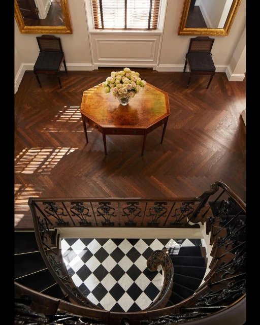 Overhead shot of a grand entryway with dark wood floors, a spiral staircase, and a table topped with a bouquet of flowers.