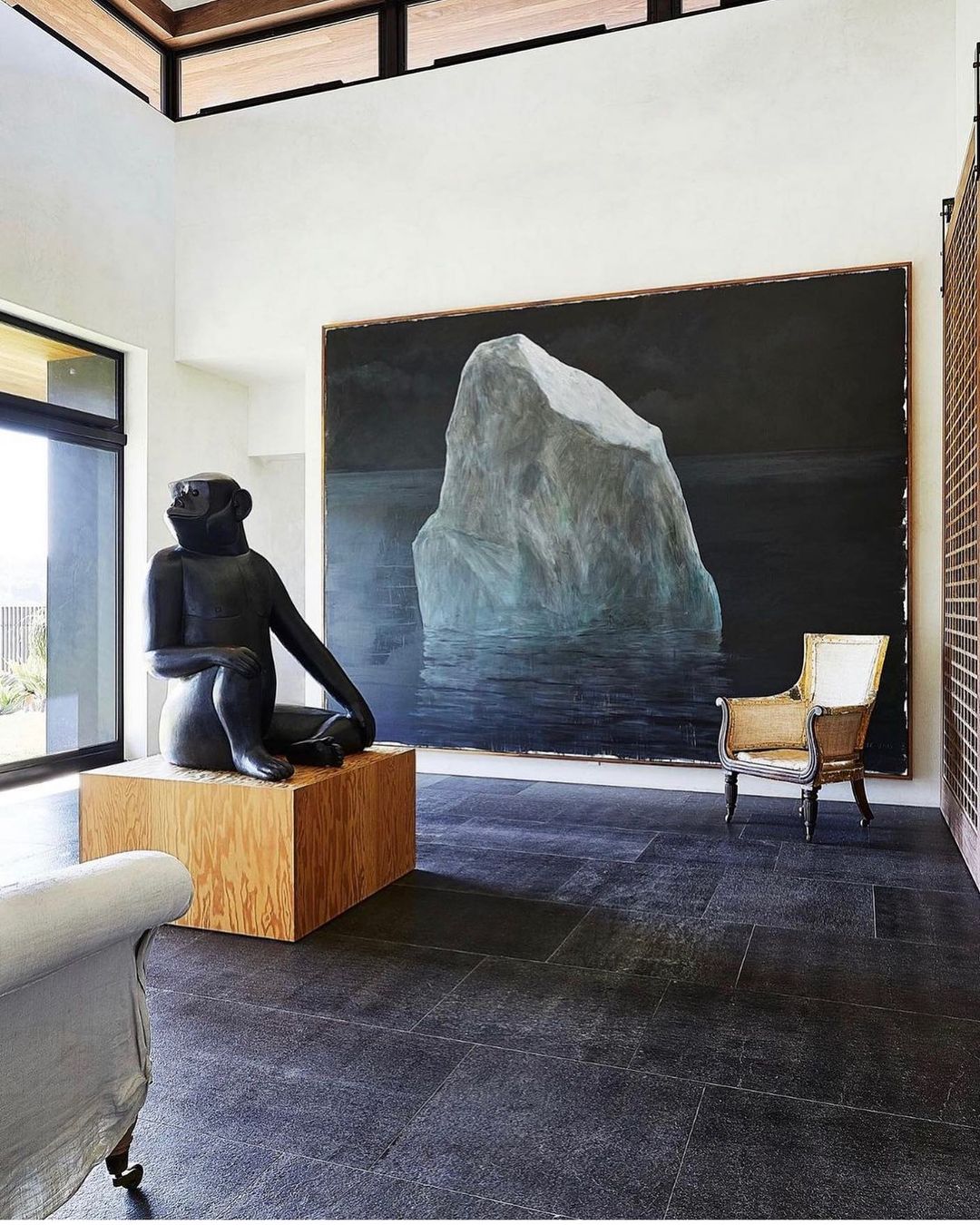 Interior of a modern living room with a sculpture of a seated monkey on a wooden pedestal, and a painting of an iceberg on the wall.