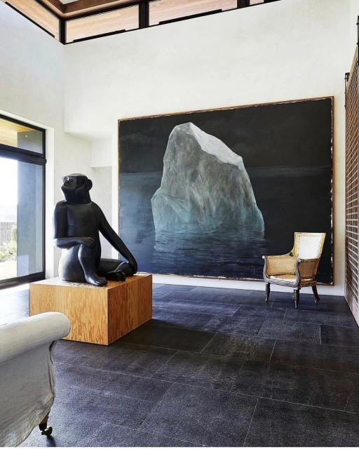 Interior of a modern living room with a sculpture of a seated monkey on a wooden pedestal, and a painting of an iceberg on the wall.
