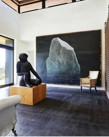 Interior of a modern living room with a sculpture of a seated monkey on a wooden pedestal, and a painting of an iceberg on the wall.
