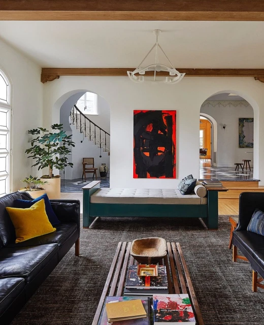 A living room interior featuring a black leather sofa, a modern coffee table with books, and abstract art on a white wall. 