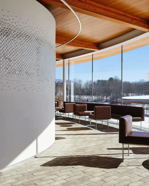 Architectural interior of a modern lounge with brown leather chairs and sofas, white walls with textured design, brick floor, and large windows.