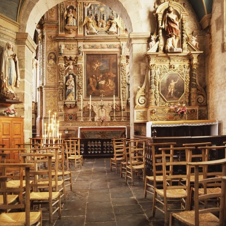Interior view of a church sanctuary with rows of wooden chairs, ornate carved altars, religious artwork, and stone archways.