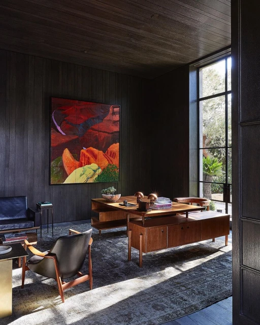 Modern interior design showcases a home office with a dark wood desk, black chairs, and a contemporary painting, bathed in natural light.