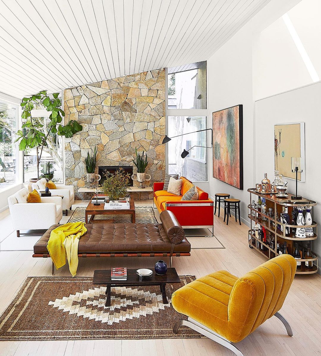 Bright living room with stone fireplace and mid-century modern furniture, including a yellow lounge chair and a brown leather daybed.