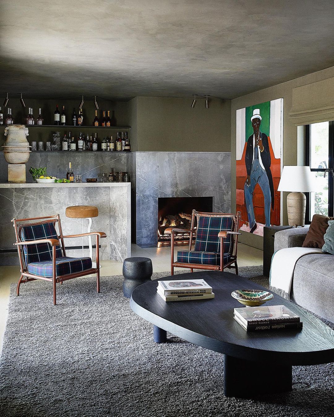 Living room interior with a gray sofa, oval coffee table, and two armchairs, a fireplace, and bar area, featuring modern design.