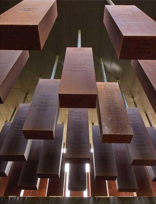 Low-angle shot showcases a memorial with rectangular, rusty-colored metal plaques suspended from the ceiling, etched with text.