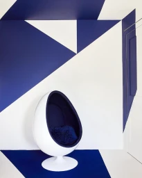 White egg chair with dark blue interior set against a wall with geometric blue and white painted triangles by William Abranowicz