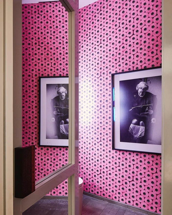 Pink patterned toilet paper wallpaper and framed black and white photographs shot through a doorway