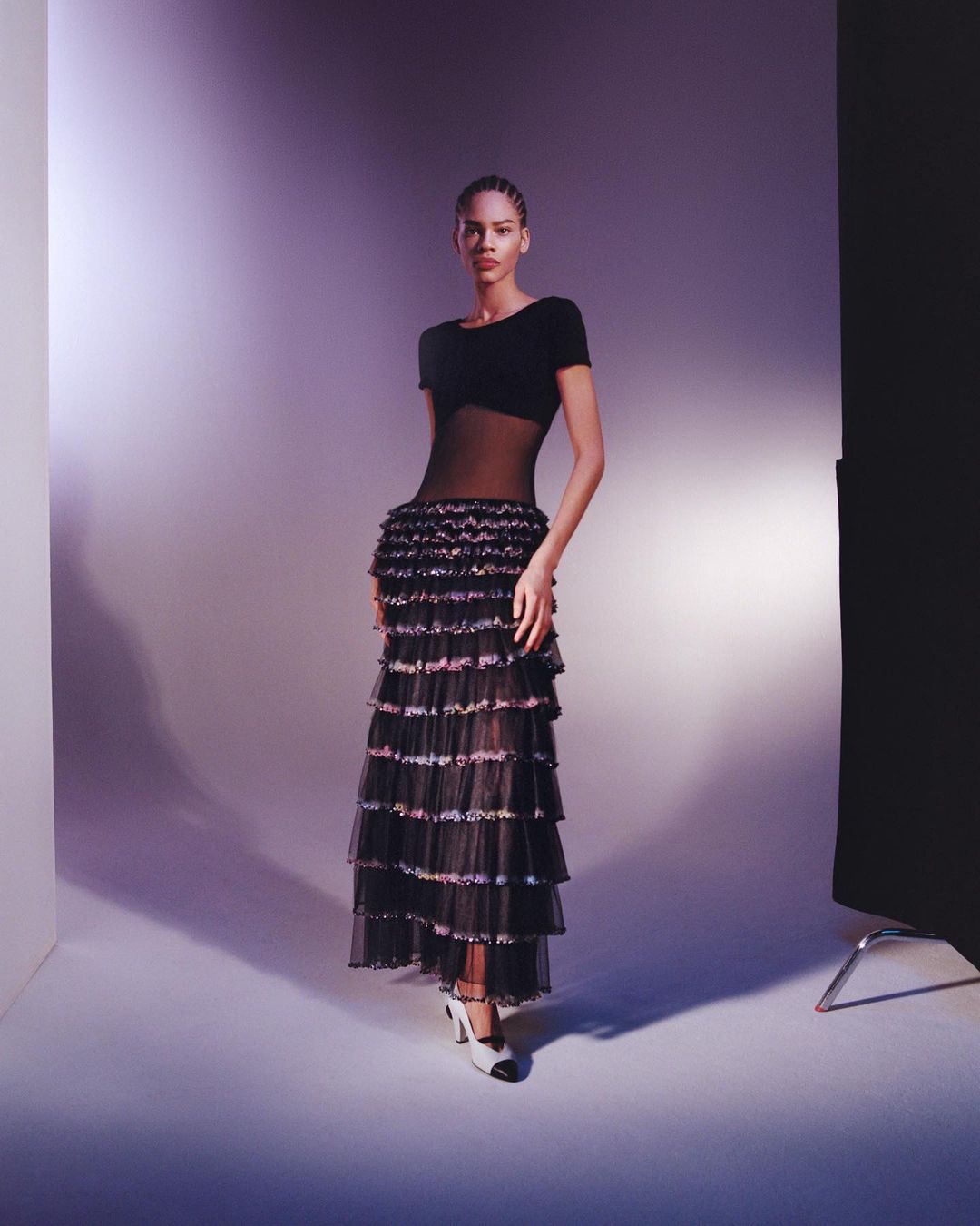 Model standing in a black sheer layered dress and white heels against a gradient studio background by William Arcand
