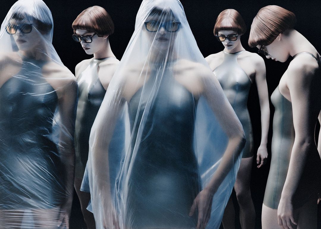 Fashion shot showcasing multiple women in gray bodysuits, some covered in plastic film, wearing sunglasses against a black background.