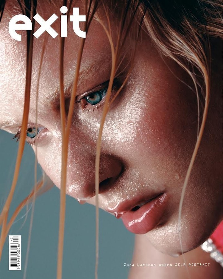 Close-up magazine cover shot of a woman with wet blond hair and water droplets on her face and shoulders, set against a grey backdrop.