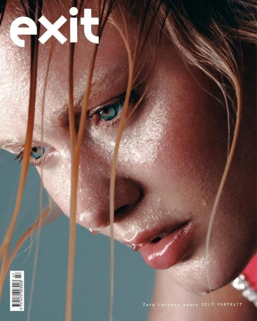 Close-up magazine cover shot of a woman with wet blond hair and water droplets on her face and shoulders, set against a grey backdrop.