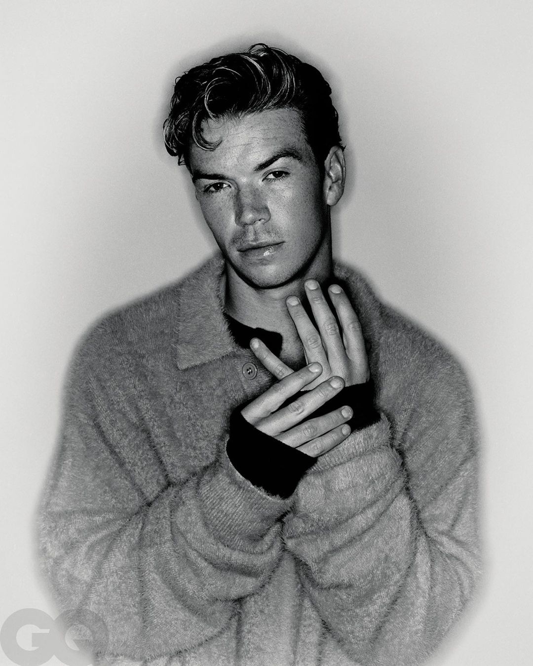 Monochrome portrait of actor Will Poulter wearing a textured knit polo sweater against a light gradient background.