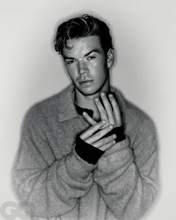 Monochrome portrait of actor Will Poulter wearing a textured knit polo sweater against a light gradient background.