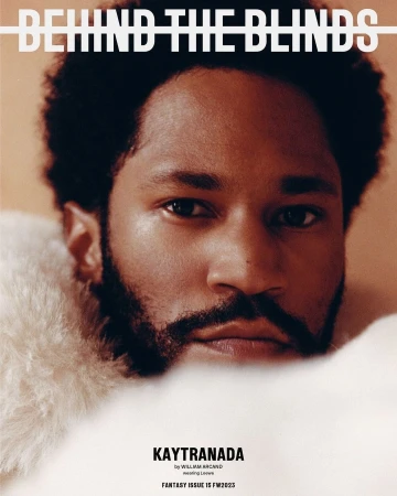 Close-up studio shot of adult male with a beard, framed by fluffy white material, featured on the cover of 'Behind The Blinds'.