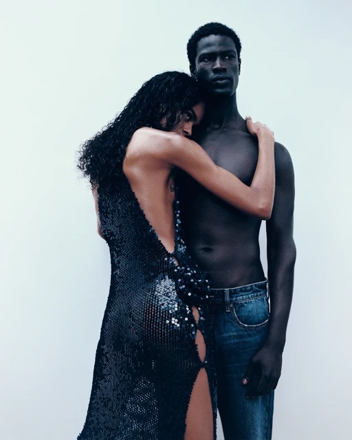 Striking studio shot of an embracing interracial couple: a Black man with bare torso and a woman in a black sequined dress.