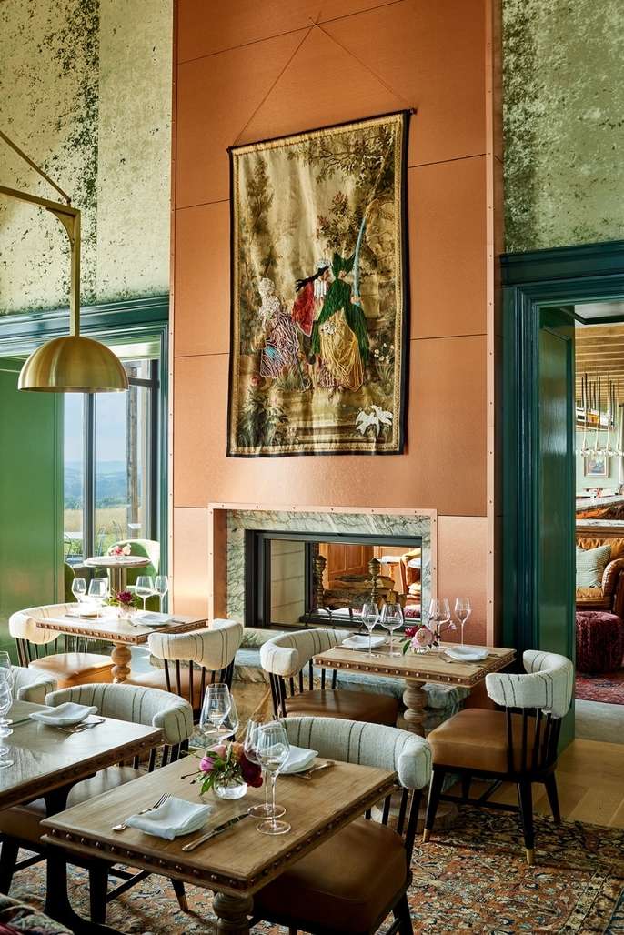 Dining room interior with set tables, wooden chairs, and tapestry on the wall above the fireplace in a stylish restaurant.