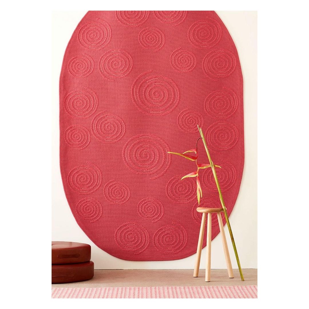 Interior still life featuring a coral-colored patterned rug with a wooden stool and ornamental flower, creating a minimalist scene.