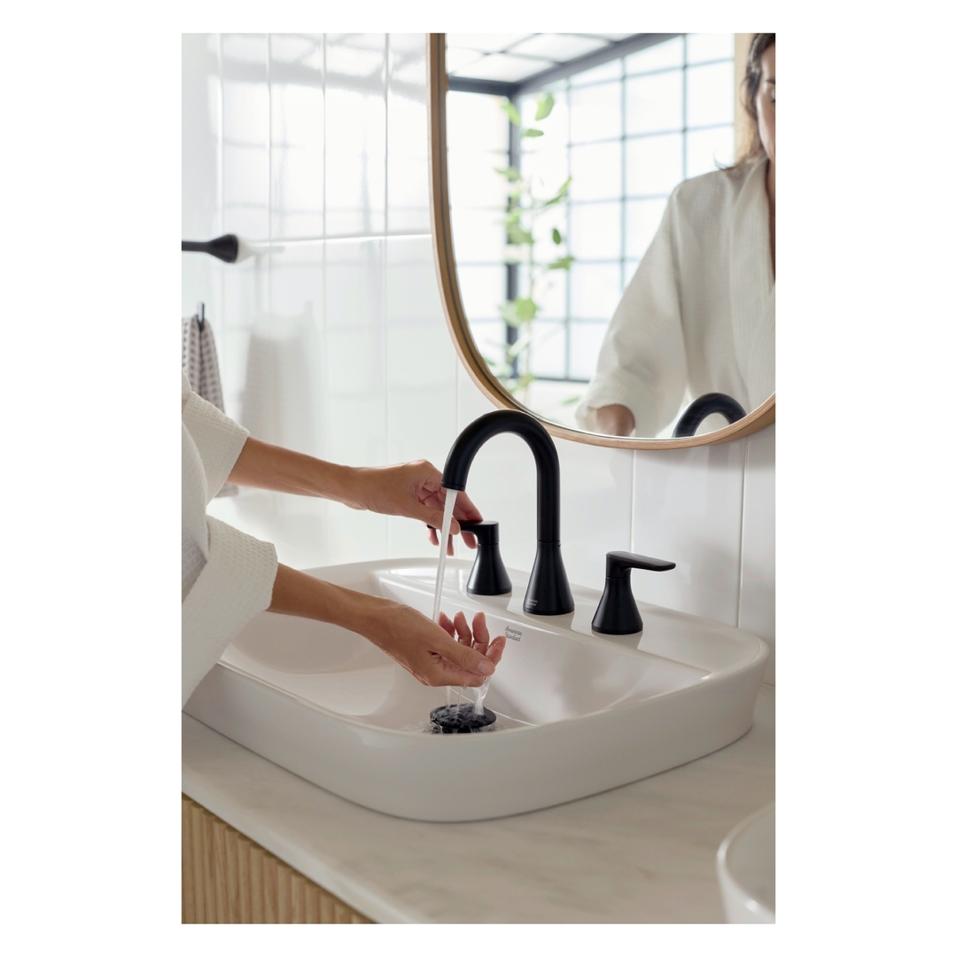 Woman washing hands at a modern bathroom sink with a black faucet and white basin, reflecting in a round mirror.