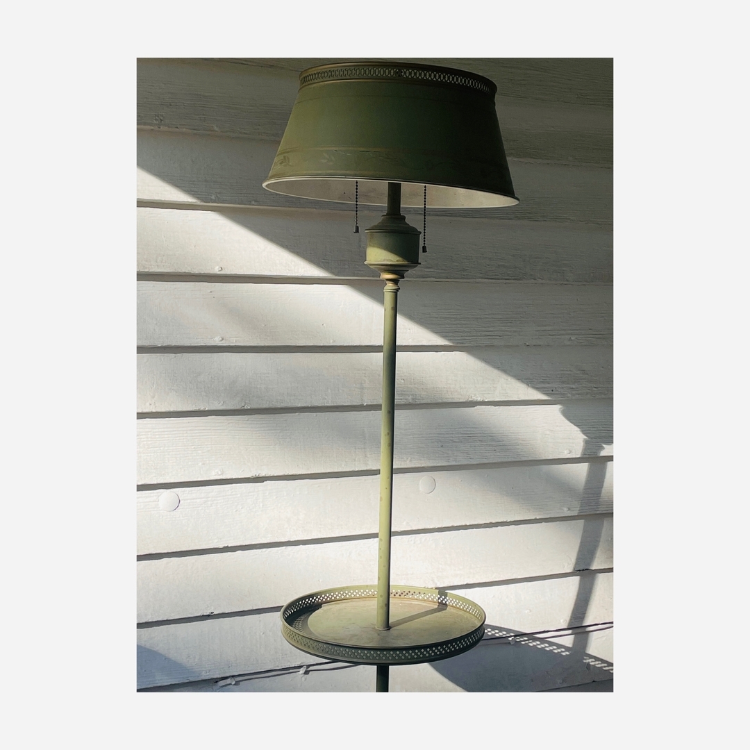 Green floor lamp stands against a white wooden wall, casting a shadow, in an indoor setting with natural lighting.