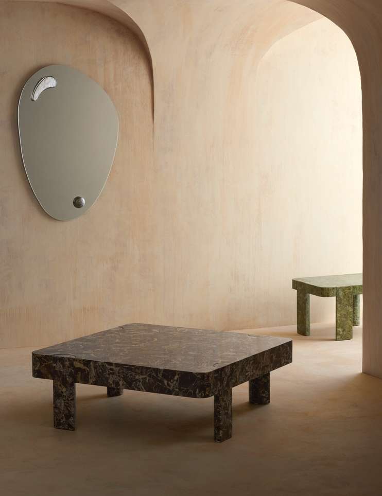 Interior design featuring a modern living room with a marble coffee table and a unique-shaped mirror on a peach-colored wall.