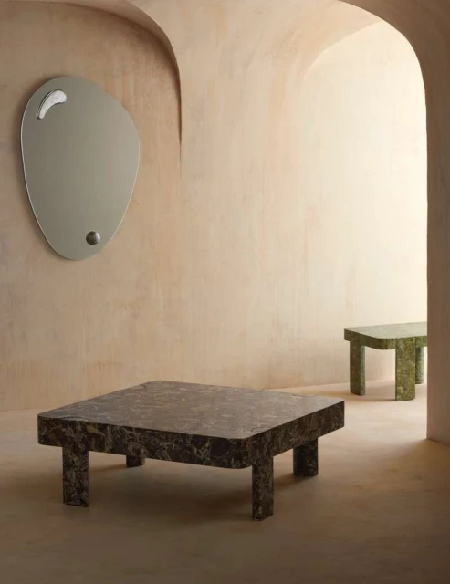 Interior design featuring a modern living room with a marble coffee table and a unique-shaped mirror on a peach-colored wall.
