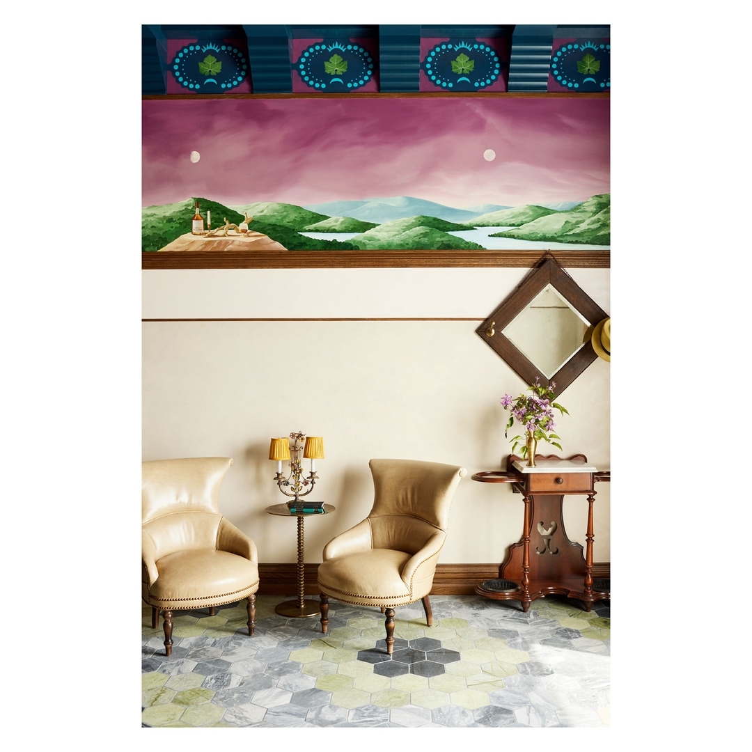 Interior design of a room featuring two upholstered chairs, a side table with a lamp, and a landscape painting on the wall.