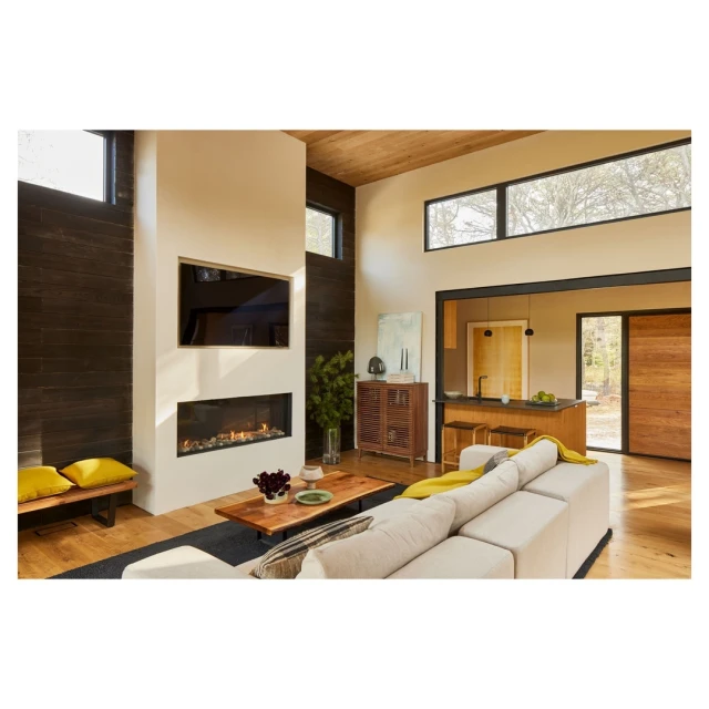 Interior of modern living room with fireplace, sofa, television, and view into kitchen; abundant natural light from large windows.