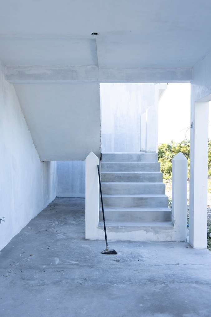 Concrete steps lead upwards in an indoor space, a broom leaning to the side, against a backdrop of natural light and greenery.