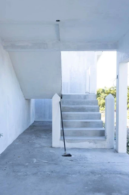 Concrete steps lead upwards in an indoor space, a broom leaning to the side, against a backdrop of natural light and greenery.