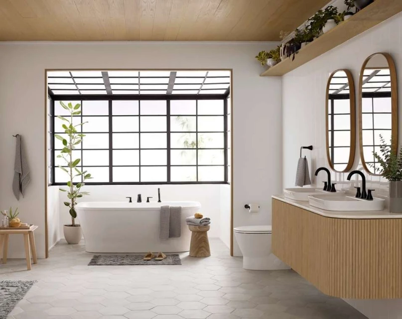 Modern bathroom interior with white bathtub, double sinks, wood vanity, geometric floor tiles, black window frame, and indoor plants.