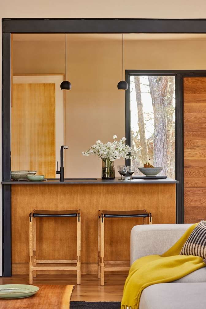 Contemporary kitchen and living area featuring modern bar stools at the breakfast bar, sleek black fixtures, and ample natural light.