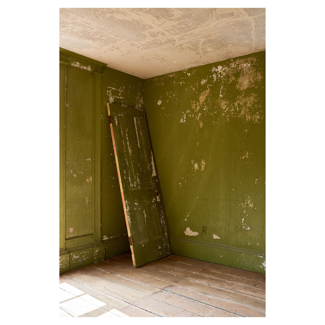 Interior of an empty room with green walls and wooden floors, featuring an old wooden door leaning against the wall.