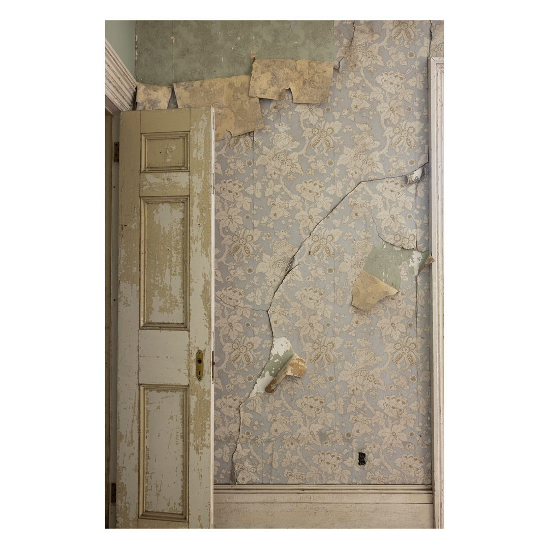 Interior view of a room with peeling wallpaper, a weathered doorframe, and visible signs of decay and age, showcasing aged textures.