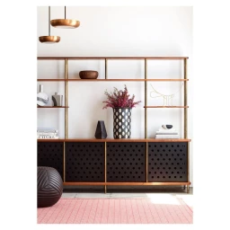 Wooden shelving unit with brass supports styled with pottery, a vase with pink flowers, and books against a white wall.