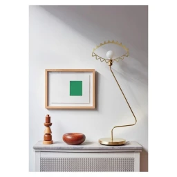 A brass eye-shaped lamp, a framed abstract green artwork, and wooden decorative objects on a pale cabinet.