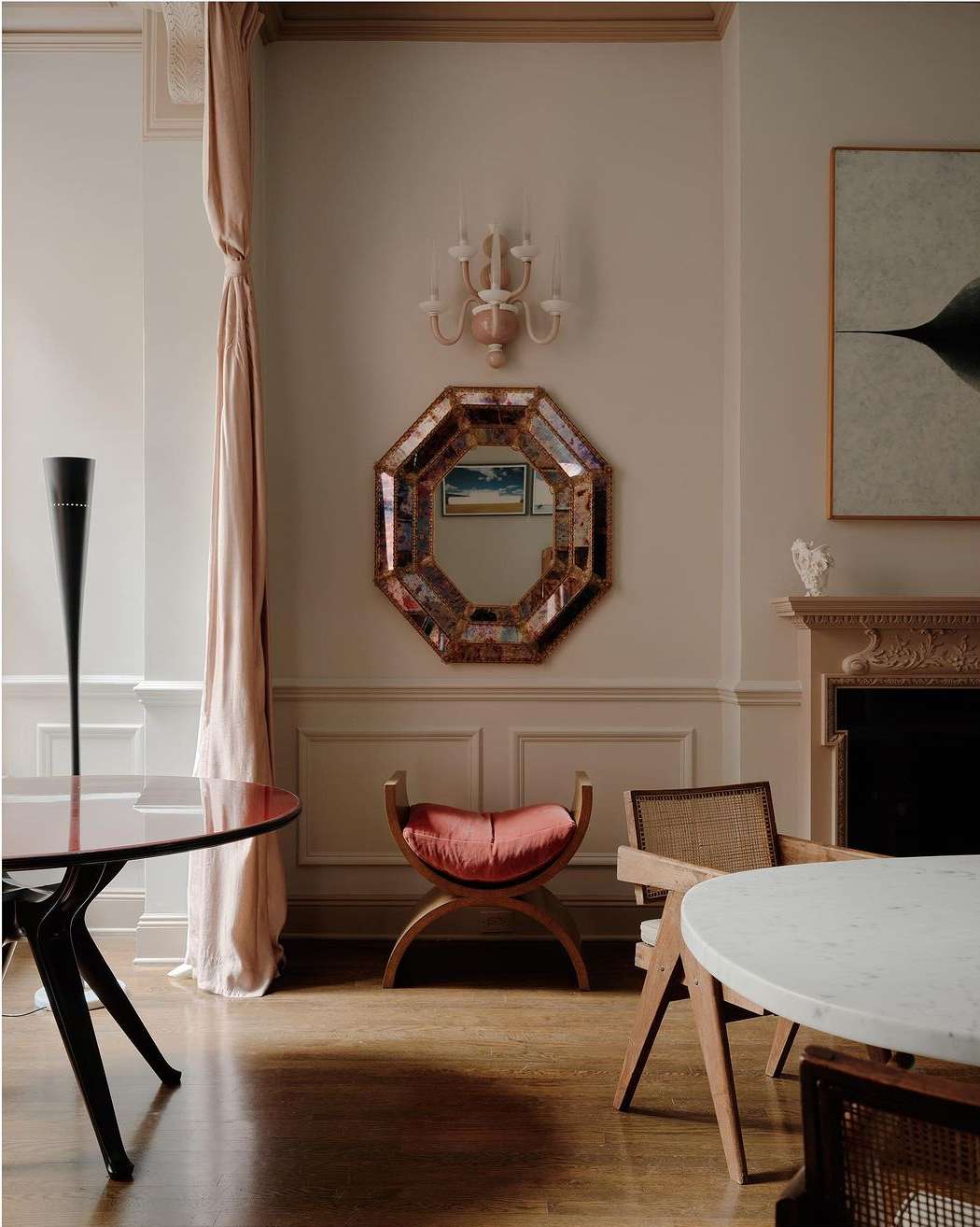 Interior design featuring chairs and tables with light pink walls, a mirror, and minimalist art above a fireplace in an elegant room.