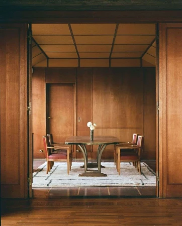 Interior view of a dining room featuring a wooden table set with white flowers, surrounded by chairs on a striped rug.