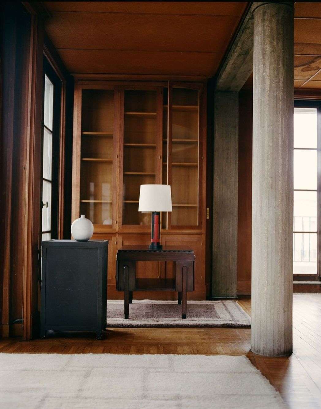 Interior view of a living space with wooden furniture, a modern lamp, a round white vase, and a neutral-toned rug on a wood floor.