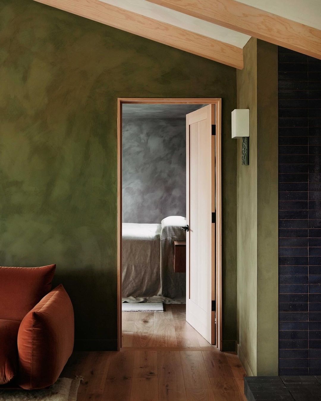Interior view of room with couch and open doorway to spa bed, showcasing earthy green tones and wooden beams in an architectural setting.