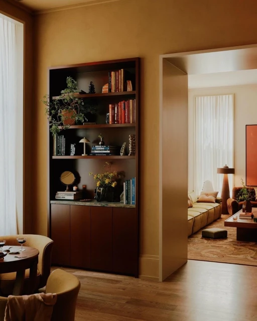Well-lit interior of a living room features a bookshelf filled with books and decorative items, complemented by seating and warm color tones.
