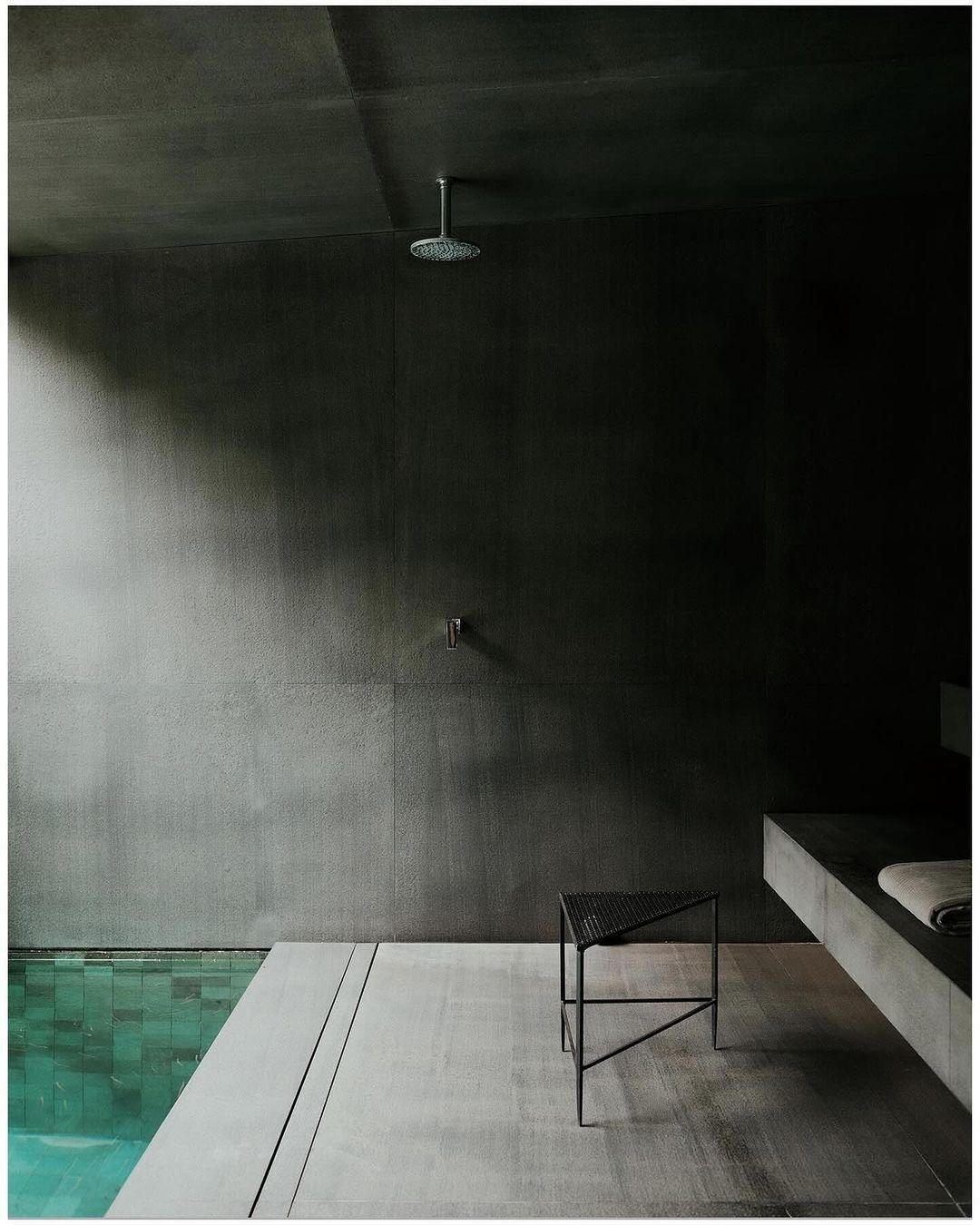 Modern bathroom interior featuring a minimalist design with dark grey walls, a walk-in shower, and a sleek metal stool, showcasing contemporary style.