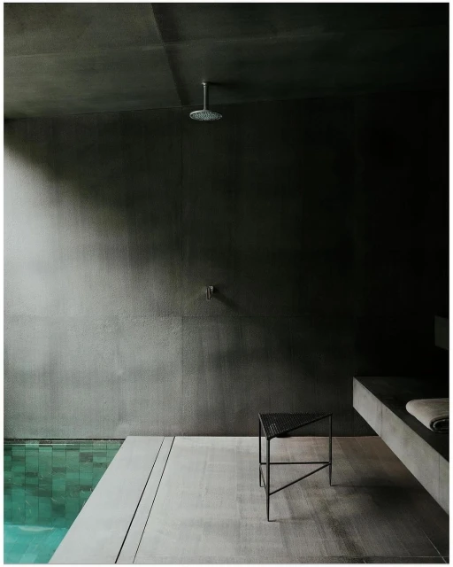 Modern bathroom interior featuring a minimalist design with dark grey walls, a walk-in shower, and a sleek metal stool, showcasing contemporary style.